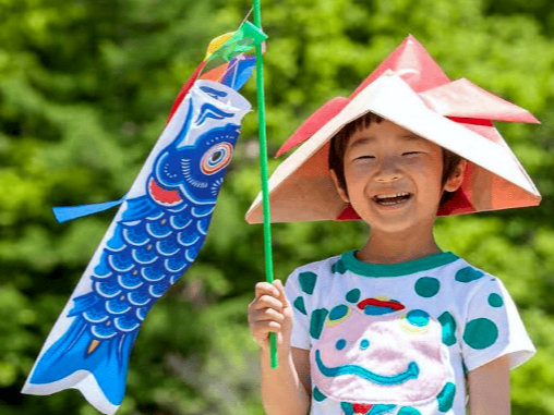 Enfant tenant un koinobori et portant un kabuto en papier pour le kodomo no hi - source Issuu.com