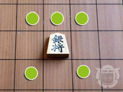 Pièce de shogi en bois sur un plateau en bois, ici le général d’argent, avec son déplacement indiqué par un symbole vert