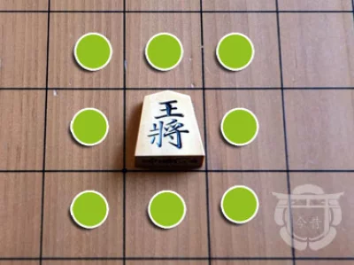 Pièce de shogi en bois sur un plateau en bois, ici le roi lance, avec son déplacement indiqué par un symbole vert