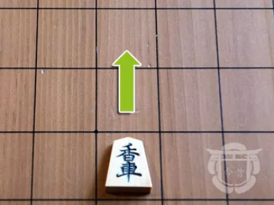 Pièce de shogi en bois sur un plateau en bois, ici la lance, avec son déplacement indiqué par un symbole vert